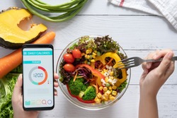 Calories counting , diet , food control and weight loss concept. Calorie counter application on smartphone screen at dining table with salad, fruit juice, bread and fresh vegetable. healthy eating