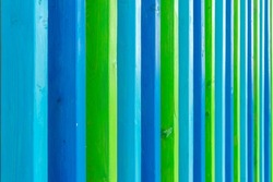 Abstract wooden fence painted in different colors. Blue-blue vertical picket fence. Striped hedge in perspective. Rhythmic color series. Decorative boards.