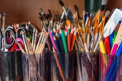 Pencils brushes scissors palette knife in cups. Accessories for fine art. Objects for drawing. Teaching children to draw. The containers are filled with stationery.