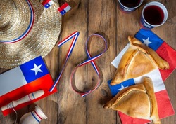 Chilean independence day concept. fiestas patrias. Tipical baked empanadas, wine or chicha, fat and play emboque. Decoration for 18 september party day, wooden background, top view.