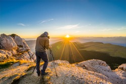 Travel photographer on top of mountain capturing sunset using DSLR camera and a tripod