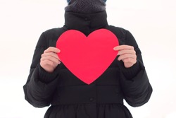 The girl on a white isolated background holds in front of her a big red horse. Figure without a face in black winter clothes. Valentine's Day stock photo with empty space for your text.