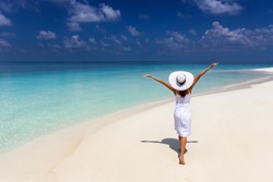 Happy traveller woman in a white dress enjoys her summer vacation on a tropical beach