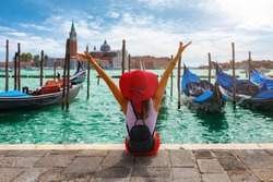 Happy traveller woman sits in front of the traditional gondolas of St. Mark's Square in Venice, Italy