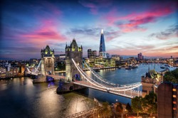 Aerial, panoramic view to the lit Tower Bridge and skyline of London, UK, along the Thames river during dusk time