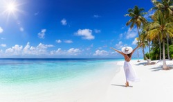 A tropical travel concept banner with copy space showing a woman in white dress walking down a paradise beach with palm trees and turquoise sea