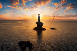 A lighthouse on a steep rock within the calm, mediterranean sea of Greece during summer sunrise, Andros island, Cyclades