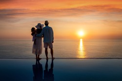 A hugging family on summer holidays enjoys the beautiful sunset over the sea by the swimming pool
