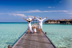 A happy family in white summer clothing on vacation walks along a wooden pier over tropical, turquoise ocean in the Maldives, Indian Ocean