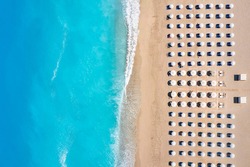 Top view of a beach with symmetrical sunbeds and parasols next to turquoise sea as seen in Greece