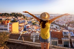 A happy tourist woman overlooks the colorful old town Alfama of Lisbon city, Portugal, and castle Sao Jorge during golden sunset time