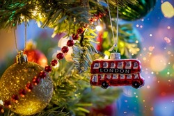A little, red double decker bus from London as a christmas ornament on a illuminated tree with selective focus