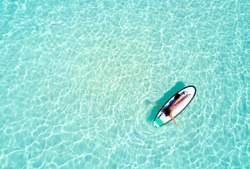 Aerial view of a woman on a surfboard in the turquoise waters of the Maldives