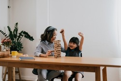 Happy exciting moments of Asian grandmother with her granddaughter playing jenga constructor. Leisure activities for children at home.