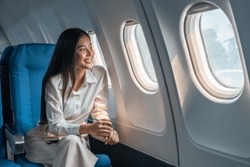Asian woman sitting in a seat in airplane and looking out the window going on a trip vacation travel concept