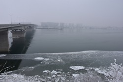 Winter landscape on the big river. Across the river is a strong concrete bridge. Along the riverbank is ice and icebergs.