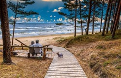 Beautiful Baltic coastal landscape and couple of seniors with a small dog are resting on sandy beach of the Baltic Sea in Jurmala - famous tourist resort in Latvia
