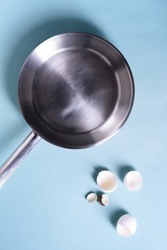 Egg shell and a cooking pan over blue table background. Healthy breakfast concept. Flat lay, view above, text space.