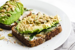 Healthy avocado toasts for breakfast or lunch with rye bread, sliced avocado, arugula, pumpkin and sesame seeds, salt and pepper. Vegetarian sandwiches. Plant-based diet. Whole food concept.