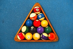 Colorful solid and striped billiard balls in a black ball rack on a blue felt pool table.