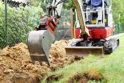 Workman using a mini digger to excavate a hole for water pipes in the garden. Czech republic, Europe.