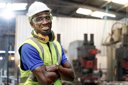 African man workers engineering standing with confident with blue working suite dress and safety helmet in front of indoor factory. Concept of smart industry worker operating.