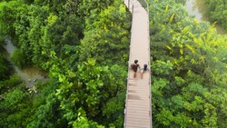 people of man and girl in top view walk at wooden sky walkway in forest with trees and river.(aerial forrest view)