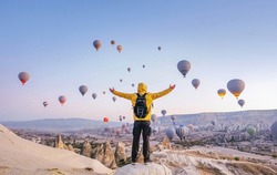 At dawn a tourist with a backpack on the background of soaring hot air balloons in Cappadocia, Turkey, concept achievement, team, leader