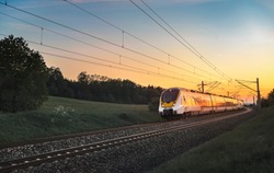 Modern regional train traveling with speed on railway tracks through nature landscape, at sunset, near Schwabisch Hall, Germany.