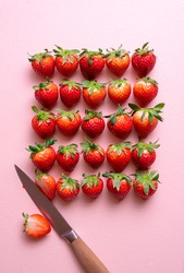 Above view with fresh strawberries arranged symmetrically on a pink table. Single sliced strawberry. Crowding concept