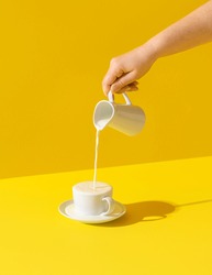 Woman pouring milk from a jug, in bright light, isolated on yellow-colored background. Milk dripping. Fresh organic morning drink. Milk over spilled.