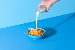 Pouring milk from a bottle into a bowl with cornflakes cereals. Bowl with corn cereals and milk isolated on a blue background