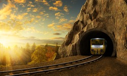 Mountain railroad with train in tunnel. Sunset landscape under the big rock.