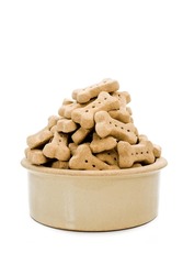 Dog Biscuits in a dog bowl against a white background. A cream ceramic dog bowl with a huge pile of dog treats filling it.
