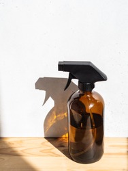 Brown glass spray bottle on wooden shelf on bright background
