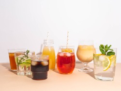 Various refreshing non-alcoholic drinks in glasses with ice. Different juice, homemade lemonade, iced coffee, iced fruit tea and smoothies on beige background. Copy space. Front view