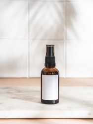 Amber bottle with white label mockup for bathing products in bathroom on marble table and white wall tile. Palm leaf shadow. Front view. Copy space
