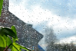 Blurred gray and blue background. Raindrops on the transparent window pane. Background of raindrops on a wet and transparent glass texture. It's raining outside. Water droplets glisten in the sun.
