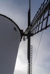 A close up vertical view of a whitewashed windmill under a blue and cloudy sky