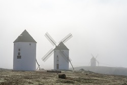 View of whitewashed windmills in La Mancha on a foggy morning