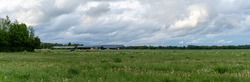 A panorama view of typical large Dutch farm with many buildings and fields under an overcast sky