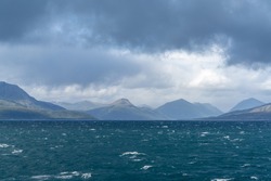 A rugged and wild coastline with mountains and stormy seas with whitecaps under and expressive cloudy sky