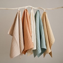 Collection of natural muslin kitchen towels are hung in a row on an unusual wooden hanger. Natural, soft, airy and stylish kitchen textiles.
