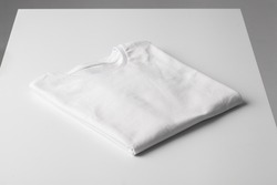 Basic folded white Tshirt on grey table. Mock up for branding t-shirt. Monochrome trend. 