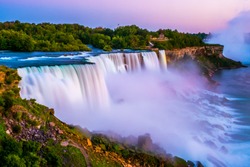 Niagara falls in the summer during beautiful evening, night with clear dark sunset blue sky. Niagara fall water hit with many colorful lights that is beautiful in a way. Sky turning dark and cold.