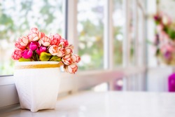 Bouquet of artificial flowers in white pot on white table near window. Selective focus.