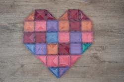 
A heart built from a magnetic building blocks. Magnetic tiles on wooden floor. Heart shaped. Magna tiles. Child's play. Pastel colors. 