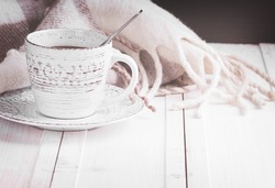 a vintage mug with hot coffee and spices decorated with a blanket in cage on a white wooden surface haze filter