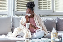 Sick day at home. African American woman has runny nose and common cold. Cough. Closeup Of Beautiful Young Woman Caught Cold Or Flu Illness. Portrait Of Unhealthy Girl Drinking Tea.
