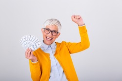 Beautiful senior lady holding a bunch of $100 bills with surprised facial expression. Mature woman winning money. Finances and people concept, senior woman holding hundreds of dollar money banknotes